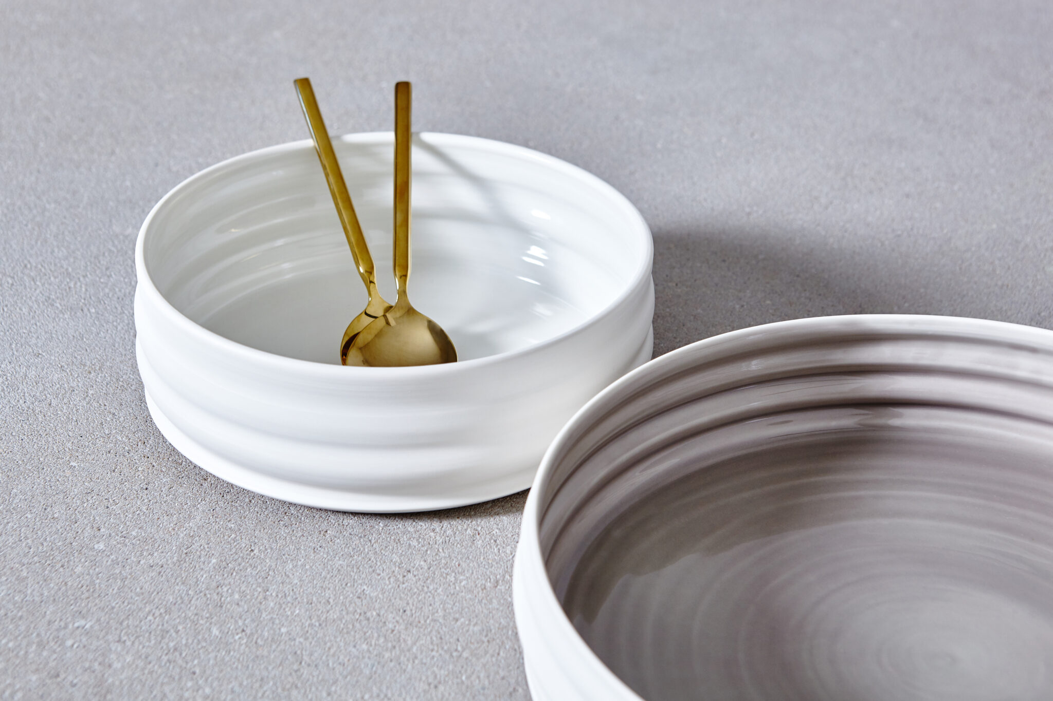 Weiße Keramikschalen von aestone ceramics mit goldenem Besteck auf grauem Untergrund