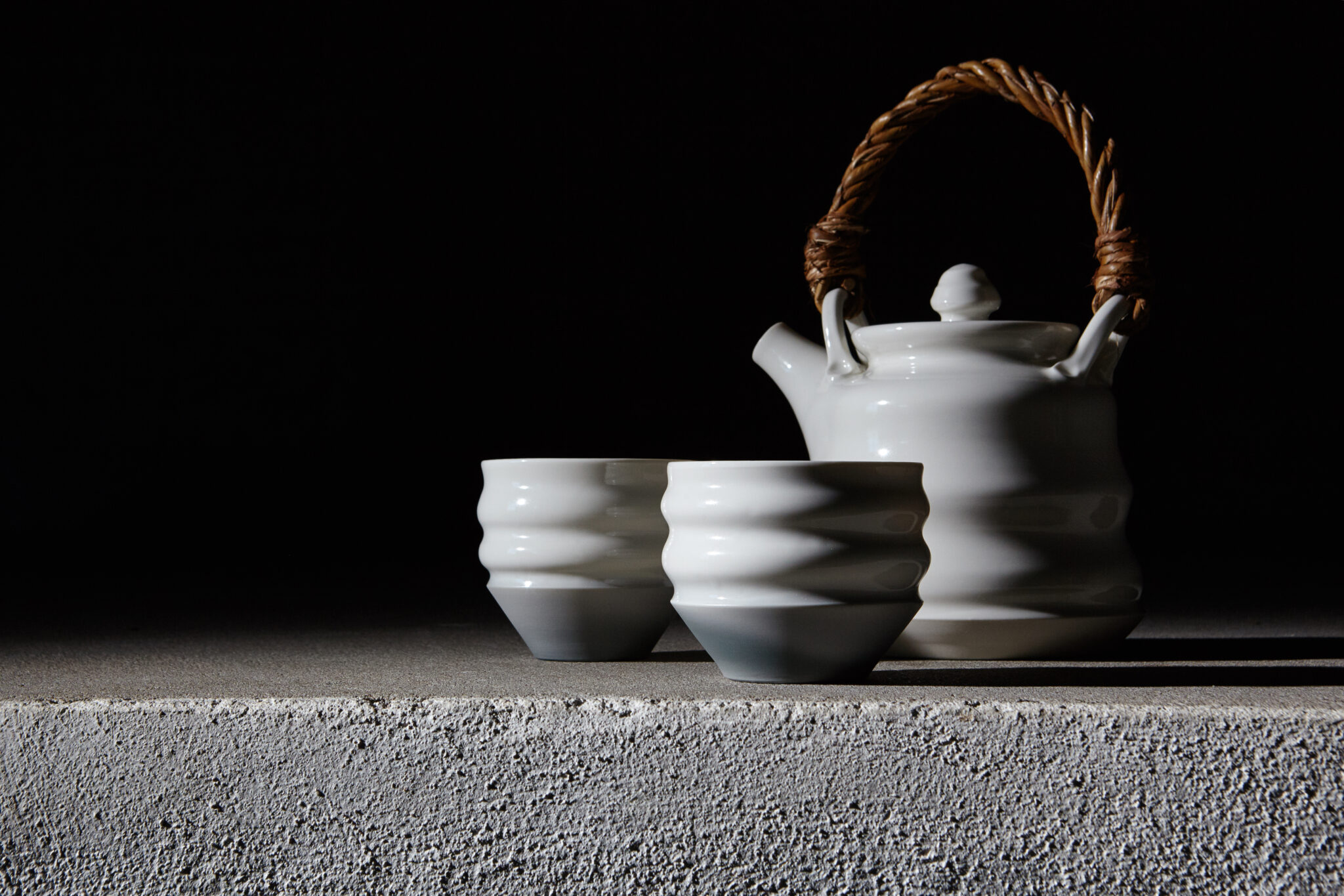 Weiße Keramik-Teekanne mit zwei Bechern von aestone ceramics vor dunklem Hintergrund