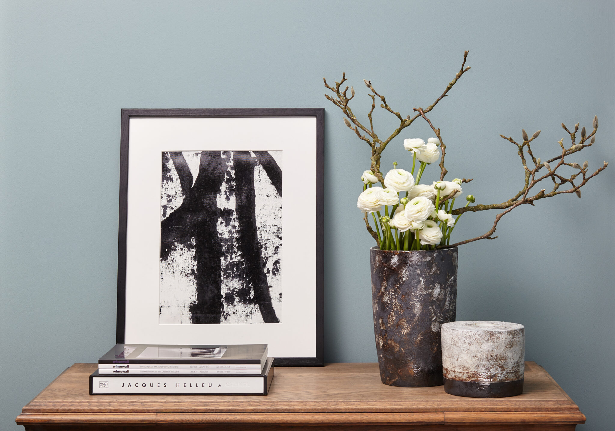 Dunkle Keramikvase mit weißen Blumen und kleines Keramikgefäß auf einer Holzkommode