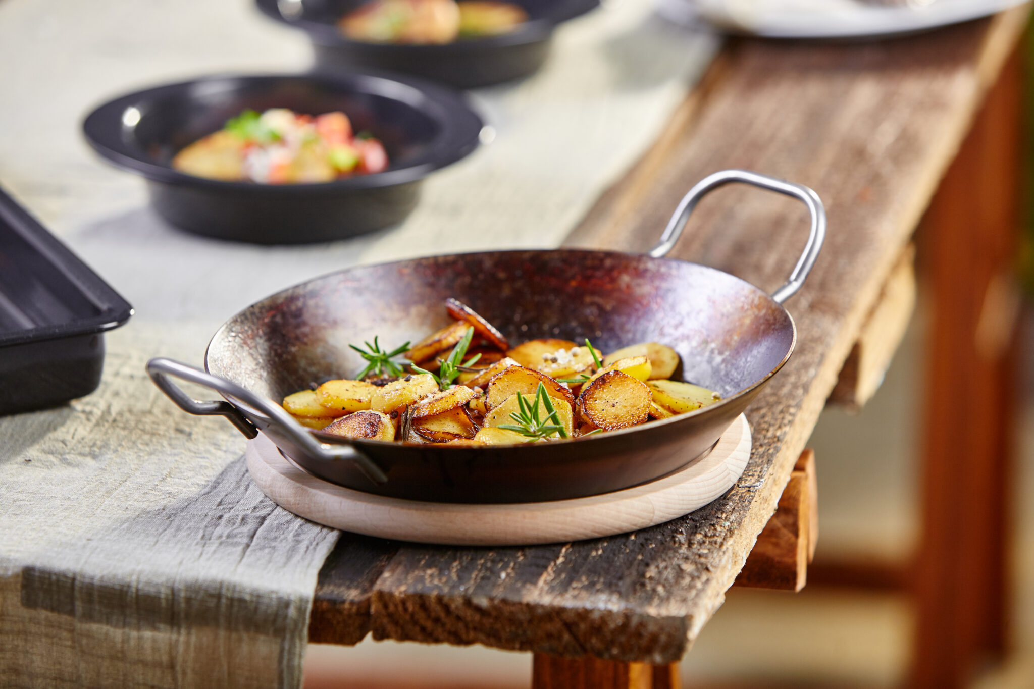Servierpfanne mit gebratenen Kartoffeln und Rosmarin auf einem rustikalen Holztisch