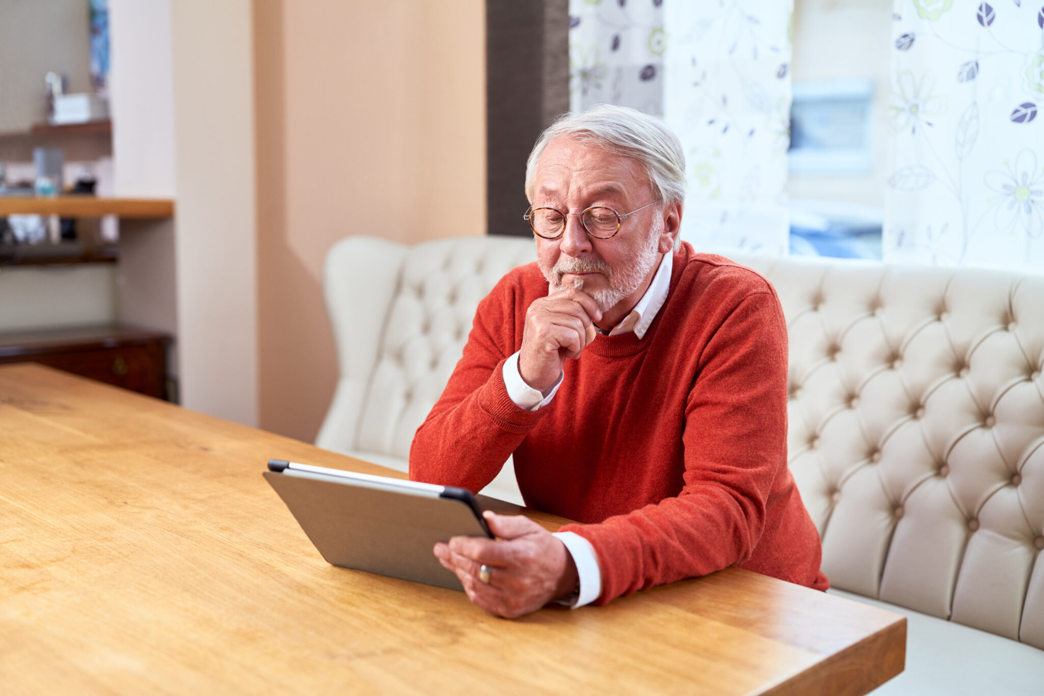 Älterer Mann sitzt mit einem Tablet an einem Tisch