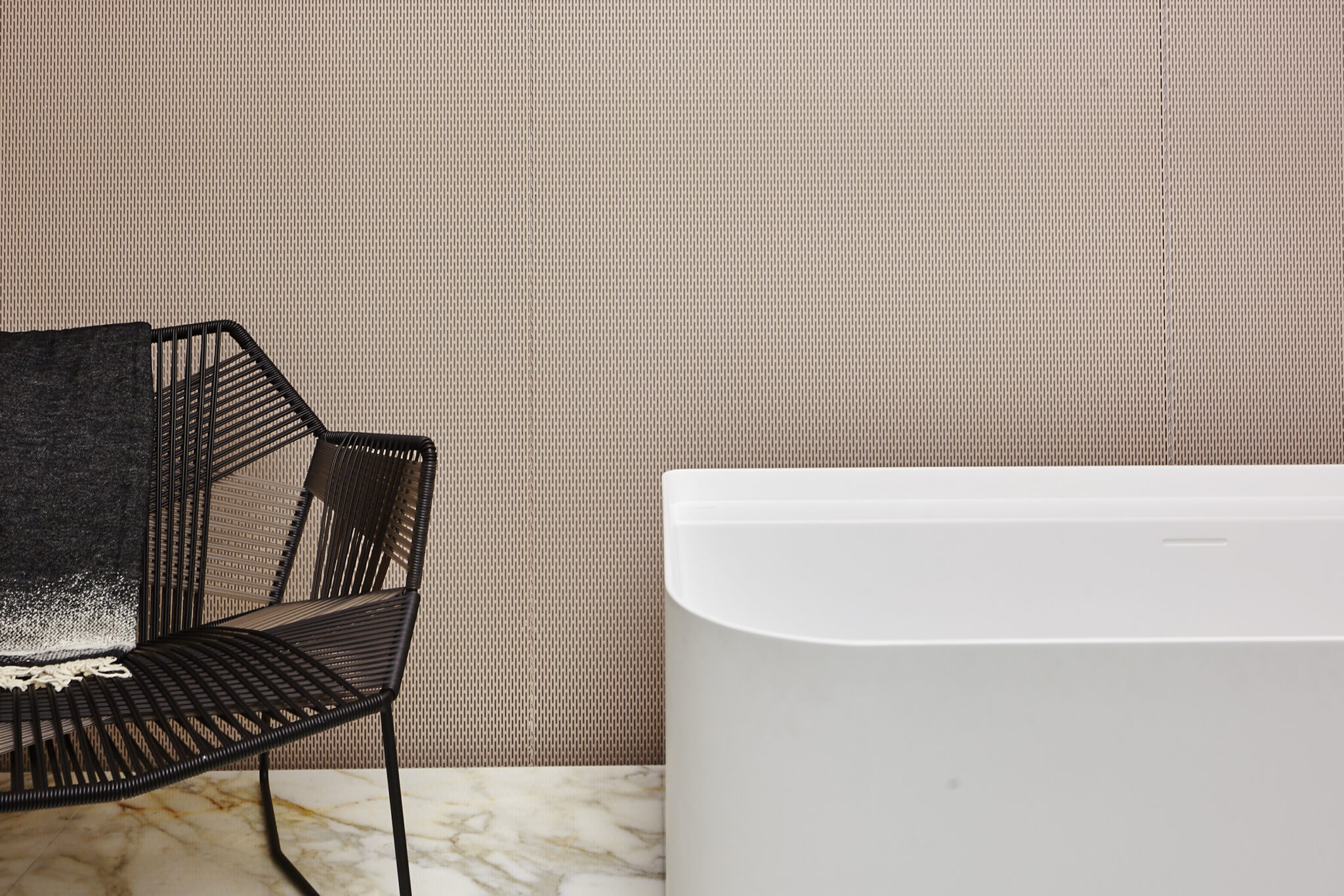 Detail eines Badezimmers mit weißer Badewanne, schwarzem Sessel und gemusterter Wand