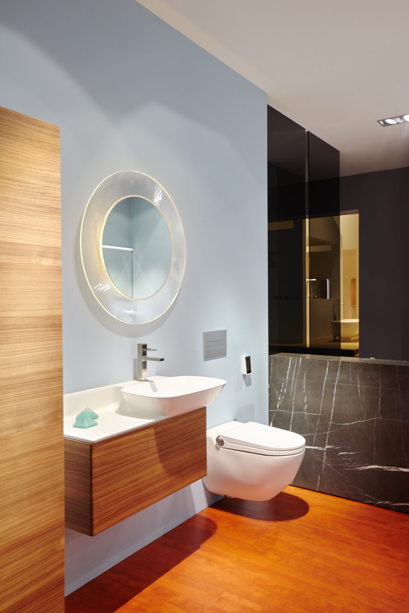 Modernes Badezimmer mit weißem Aufsatzwaschbecken, Wand-WC und rundem beleuchtetem Spiegel