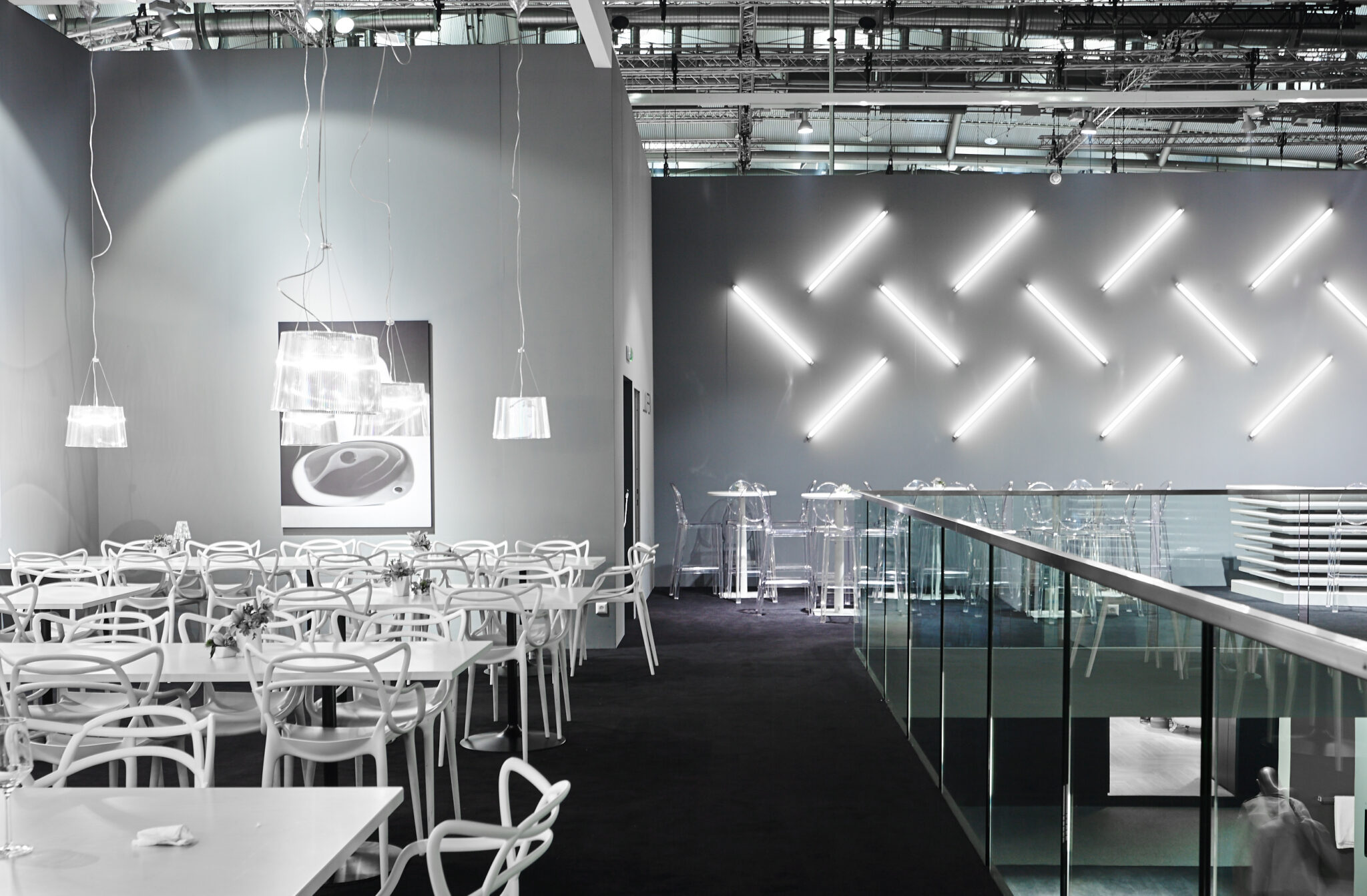 Gastronomiebereich im LAUFEN-Showroom mit weißen Tischen, transparenten Stühlen und diagonaler Lichtinstallation