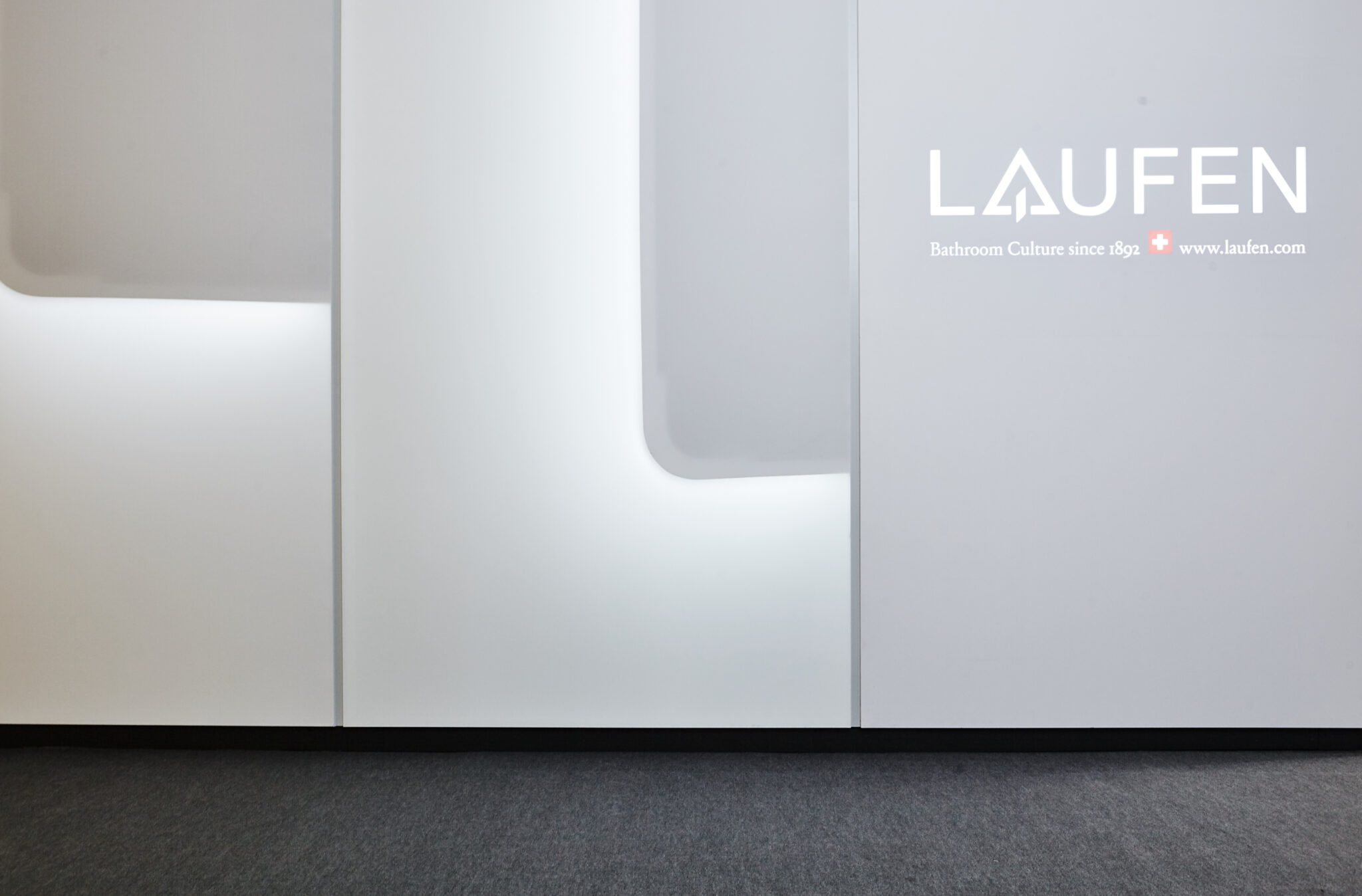 Weiße Markenwand im LAUFEN-Showroom mit beleuchtetem Logo und eingelassenen Wandflächen