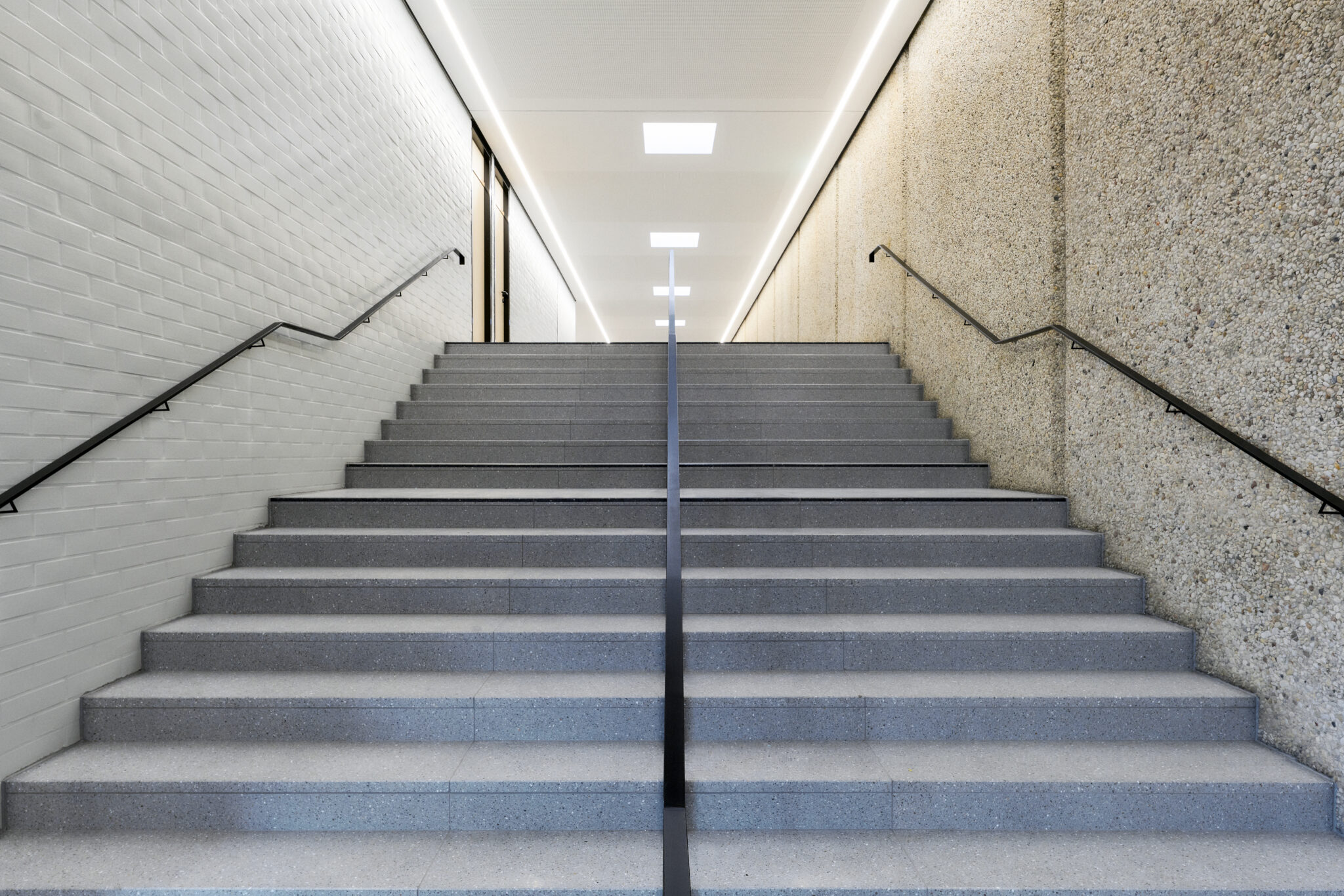 Breiter Treppenaufgang der Sporthalle II zwischen heller Klinkerwand und strukturierter Wand