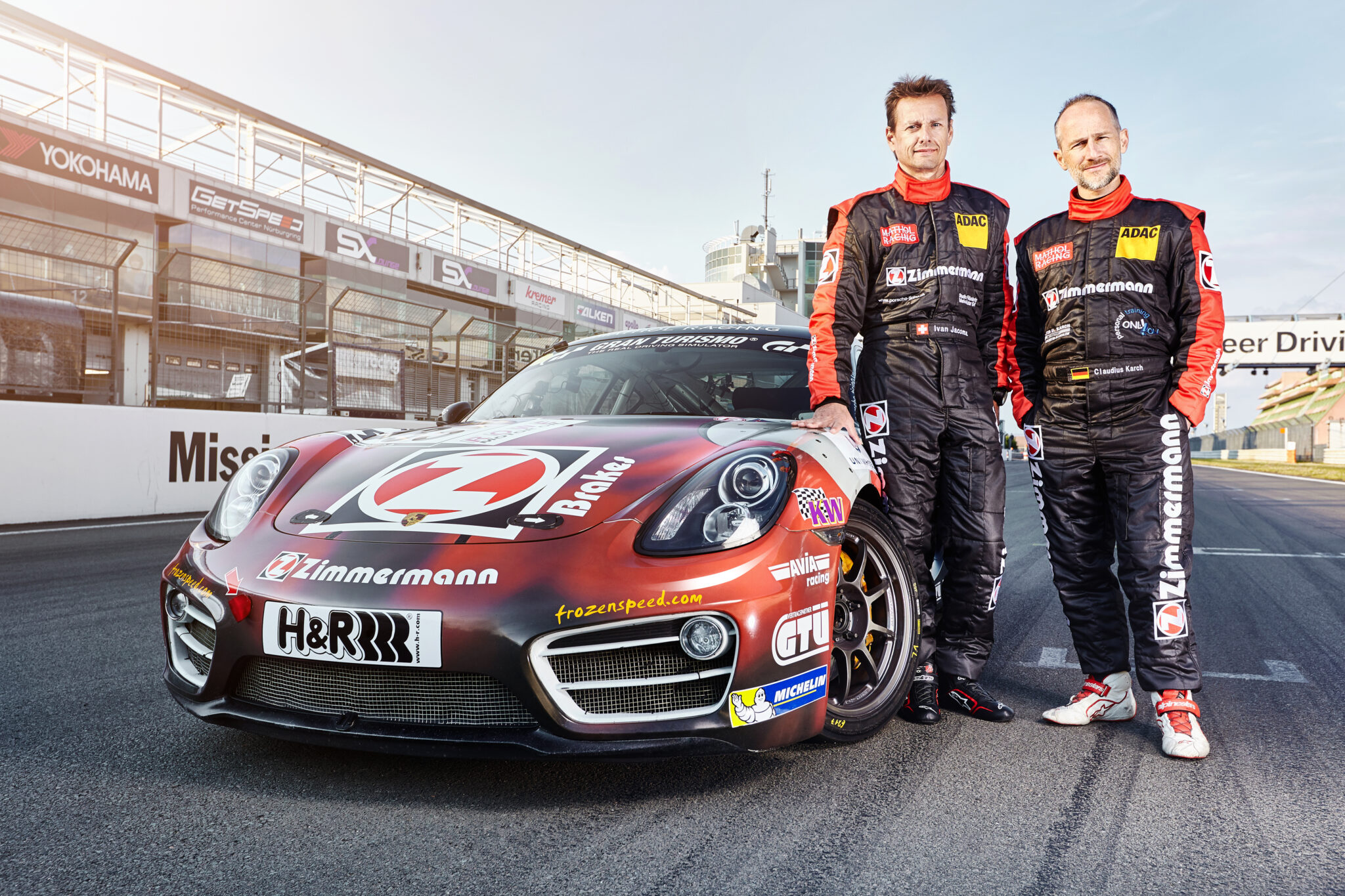 Zwei Rennfahrer neben einem Porsche-Rennwagen mit Zimmermann-Branding auf der Rennstrecke