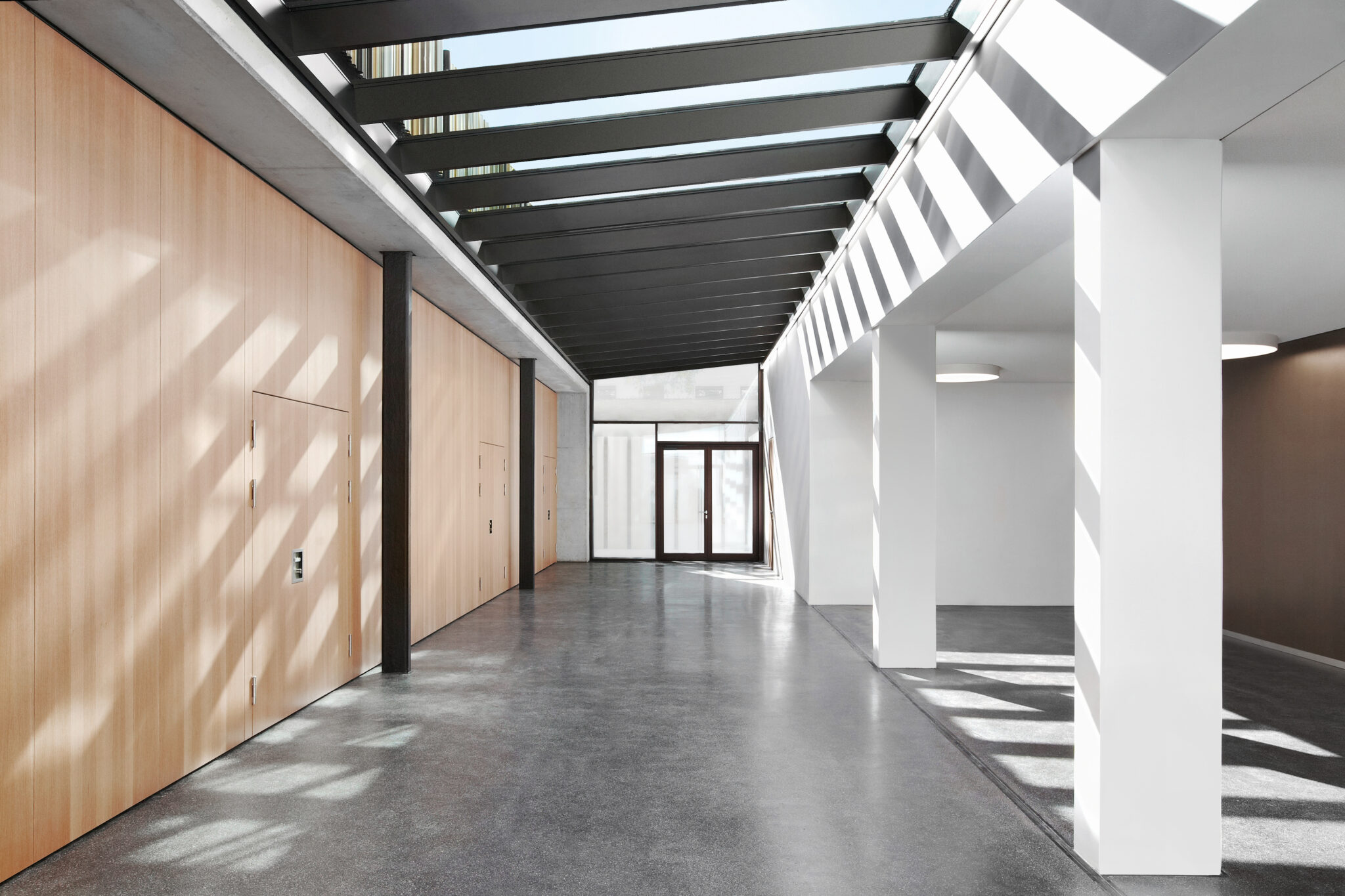 Heller Innenraum im Bischöflichen Cusanus-Gymnasium mit Glasdach, Holzwand und starken Lichtschatten